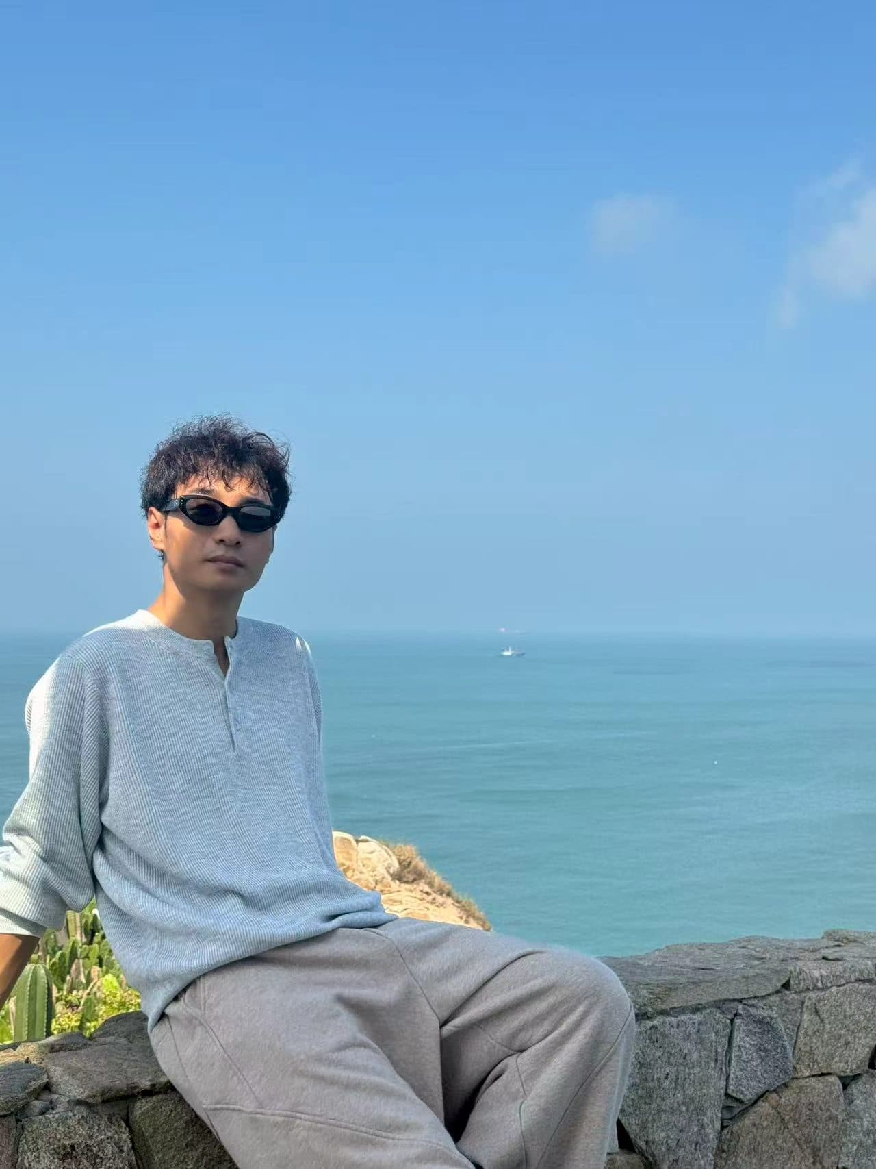 佩戴 GANZER 黑色镜框的男士坐在海边